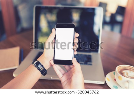 girl using smart phone in cafe. hand holding smart phone white screen. black color smart phone vintage tone. hand holding using mobile phone in coffee shop