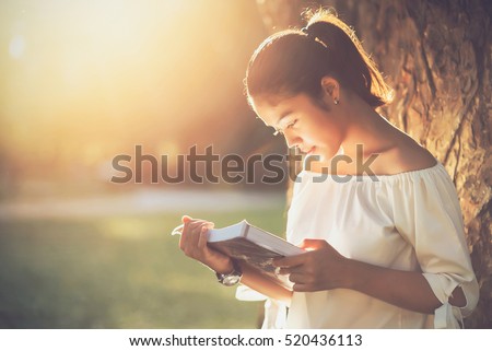 Asian girl reading book at park in summer sunset light. asian woman reading book in Thailand. asian Beautiful woman reading a book at big tree.