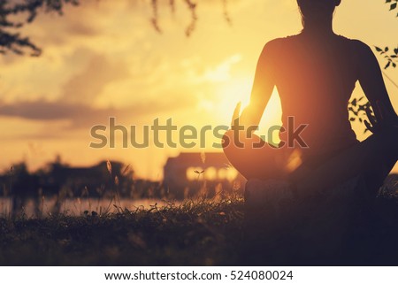 Young woman peacefully meditating in a open field. Happy young woman sitting outdoors in yoga position. Young girl practicing yoga outdoors.