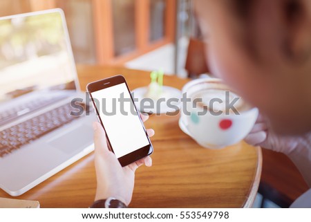 girl using smart phone in cafe. hand holding smart phone white screen. black color smart phone vintage tone. hand holding using mobile phone.