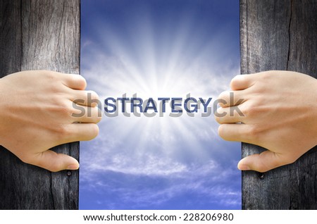 Strategy word floating and shining in the sky while two hands opening an old wooden door.