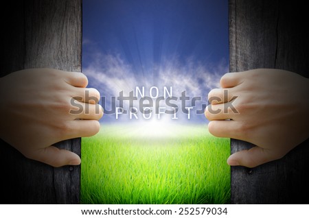 Non Profit concept. Hand opening an old wooden door and found a texts floating over green field and bright blue Sky Sunrise.