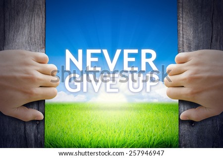 Never Give up. Hand opening an old wooden door and found Never Give up word floating over green field and bright blue Sky Sunrise.