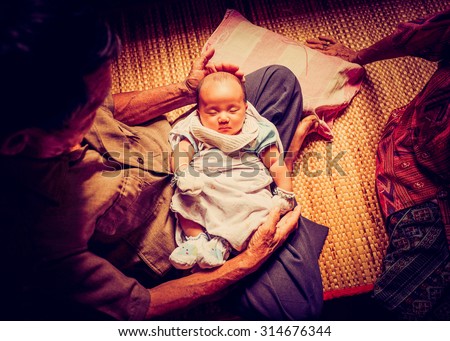The first meeting of Asian baby infant with great-grandparents. Great grand father carrying baby placed on the lap in Asian home style atmosphere.