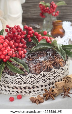 classic rich Christmas cake with berries on a top, cinnamon sticks and anise stars on a white plate