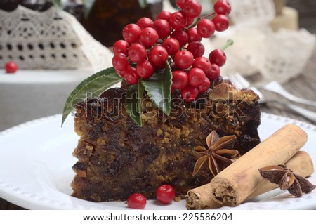 classic rich Christmas cake with berries on a top, cinnamon sticks and anise stars on a white plate