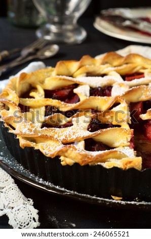 plum and mixed berries tart on a black background. selective focus
