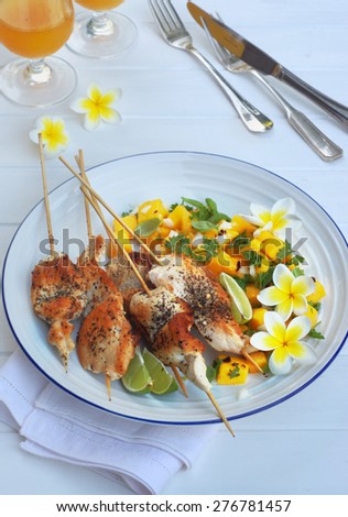 chicken skewers and mango salsa on a white round plate and white wooden background.