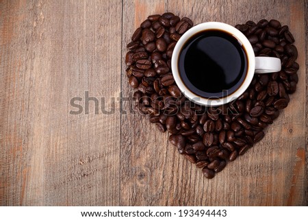 Symbol of Love, a cup of coffee in the coffee beans  isolated on Wood background