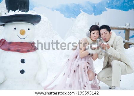 The bride and groom play in the snow, the snow beside a snowman