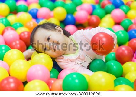 An emotional face of smiling baby playing in the balls pool. Cute and happy girl.