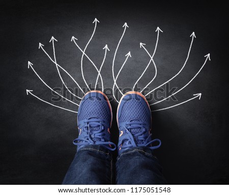 Feet with sneakers standing next to chalk arrows on blackboard taking decisions for the future