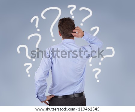 Confused businessman standing in front of a wall of question marks
