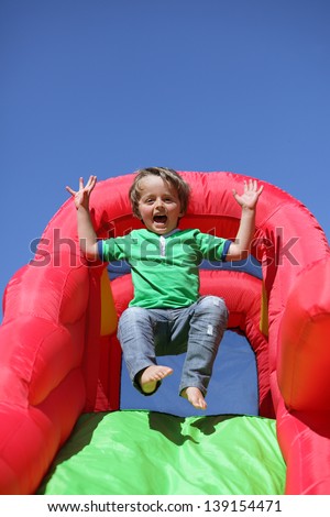 3 year old boy jumping down the slide on an inflatable bouncy castle