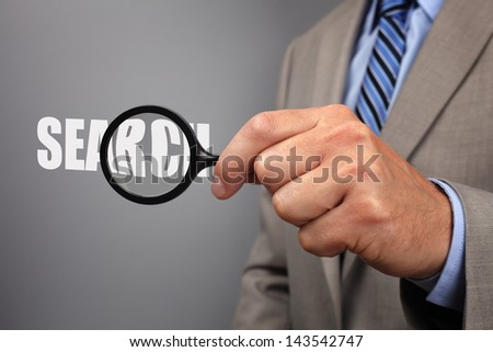 Searching businessman holding a magnifying glass across the word search