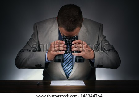 Businessman studying a contract to sign closely with binoculars concept for checking the small print