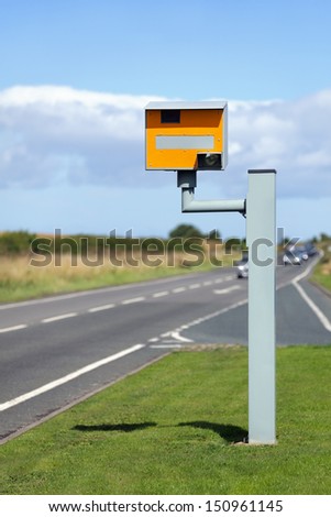 UK static speed camera with speeding cars approaching on a rural road
