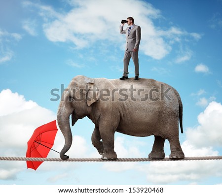 Businessman Standing On Top Of Elephant Balancing On A Tightrope Looking Through Binoculars Concept For Business Vision, Conquering Adversity Or Looking To The Future