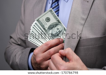 Man putting money in suit jacket pocket concept for corruption, bribing, paying or business wealth
