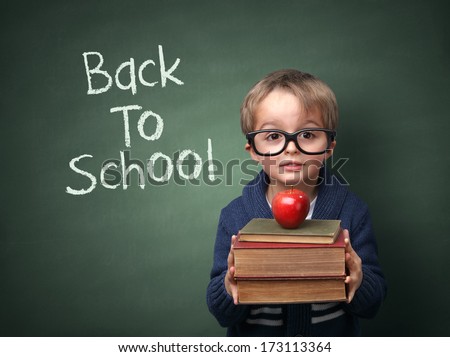 Young Child Holding Stack Of Books And Back To School Written On Chalk Blackboard