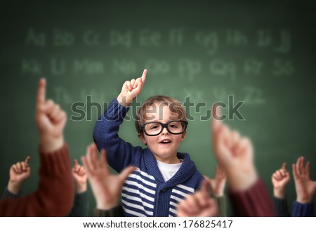 School Child With Hand Raised In The Classroom In Front Of A Blackboard With Other Children Concept For Teacher\'S Pet, Standing Out From The Crowdand, Genius Or Excelling In Education
