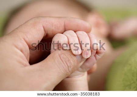 A newborn baby holds the hand of his father offering security and love