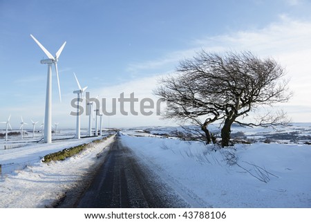Countryside road passing a wind turbine farm in winter with snow on the ground and a blue sky