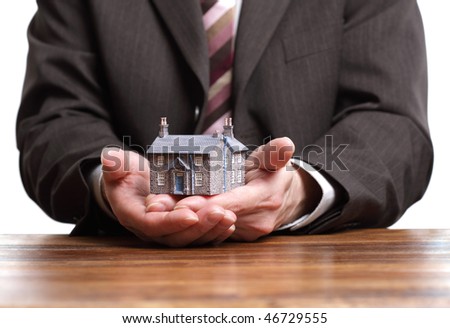Businessman or estate agent at his desk holding a model house