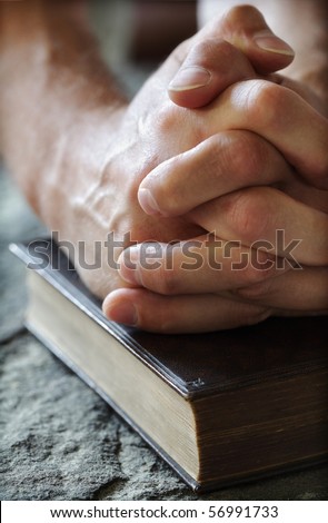 Hands folded in prayer over a Holy Bible resting on a stone baptismal font