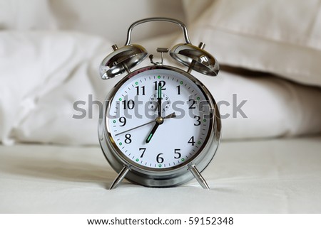 Alarm clock set to 7am ringing on an empty bed