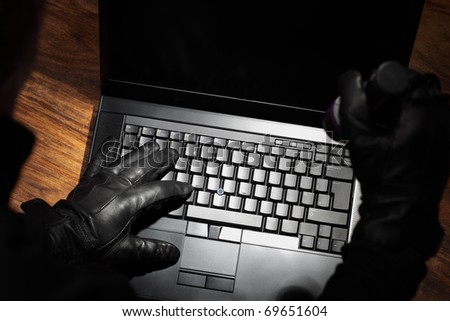 Burglar holding a torch stealing data from a laptop concept for computer security, corporate or identity theft