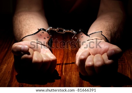 Arrested criminal hands in handcuffs on a wooden desk focus on cuffs