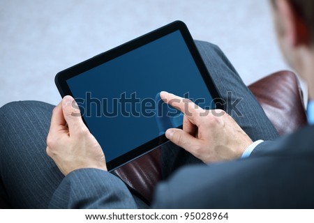 Businessman with finger touching screen of a digital tablet whilst sitting on a sofa