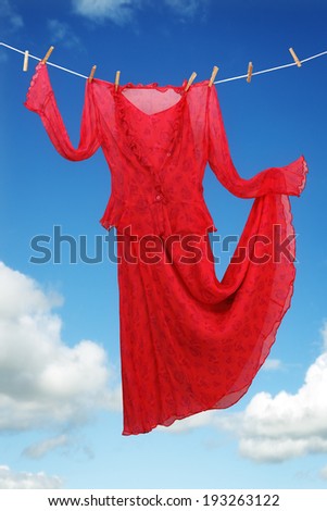 Red dress hanging and dancing on a clothesline against blue sky concept for freedom, carefree and romance
