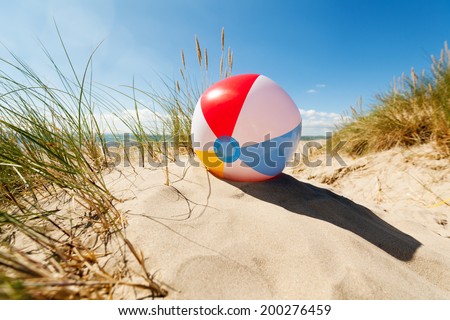 Beach ball resting in sand dune concept for childhood summer vacations, family holiday and healthy lifestyle