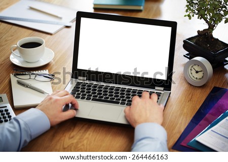 Businessman at a desk in an office typing on a laptop computer with blank white screen ready for content