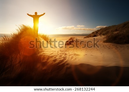 Silhouette of a man with hands raised in the sunset on a beach concept for religion, worship, prayer and praise