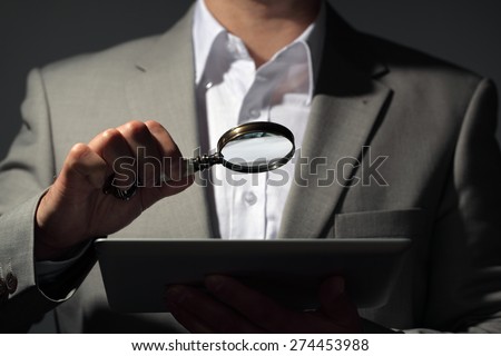 Businessman holding magnifying glass and digital tablet concept for internet search, job search or analysing accounts