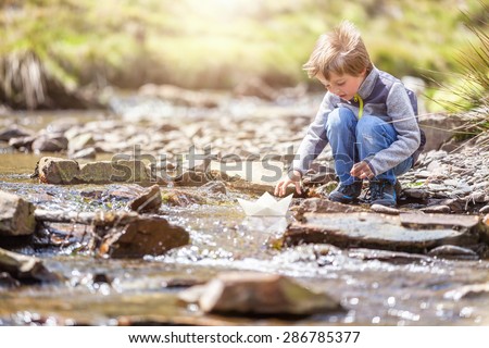 Child playing in summer sunshine with a paper boat in stream