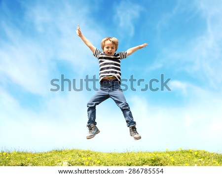 Boy jumping in a meadow at the top of a hill against a blue sky