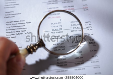Businessman holding a magnifying glass on a financial report concept for finance, balance sheet, tax or accounting