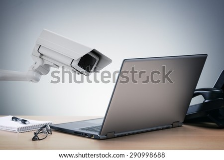 Laptop computer being watched in the office by a security camera concept for big brother surveillance or internet computer security