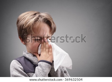 Boy suffering flu or a cold blowing his nose with a tissue