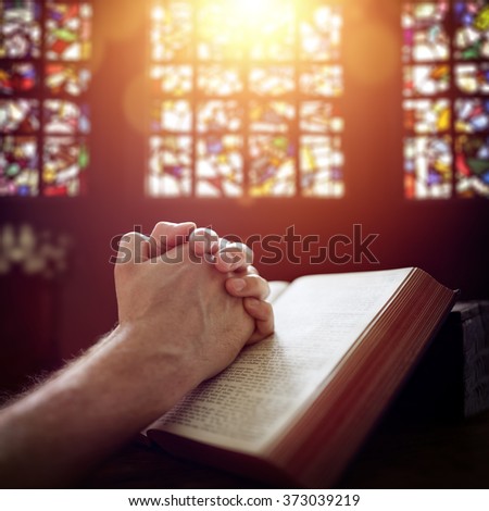 Hands folded in prayer on a Holy Bible in church concept for faith, spirituality and religion