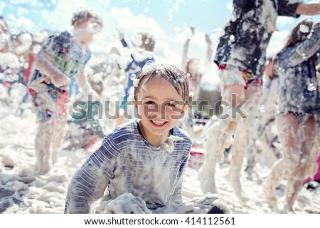 Boy smiling and laughing covered in soap suds at a summer foam party