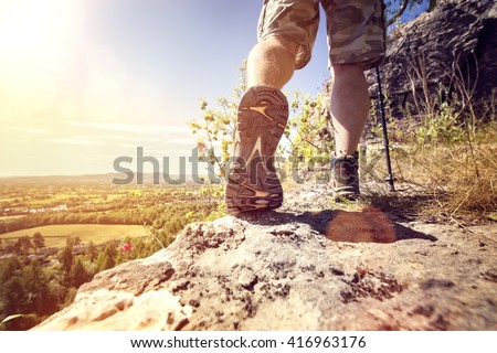 Hiker hiking on a mountain trail with distant views of countryside in summer sunshine