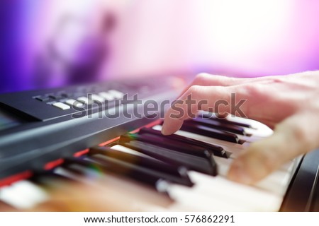 Pianist musician performing live playing keyboard in a band with saxophone player in background