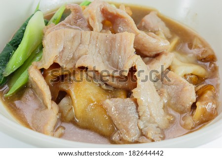 Close up to Fried noodle with pork and kale soaked in gravy, Thailand food on a white round bowl isolated over white background. Top view.