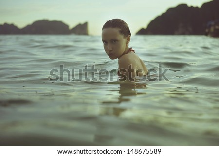 Young beautiful lady in the sea at sunset