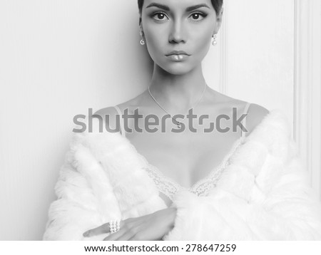 Black and white fashion photo of beautiful lady in elegant white fur coat